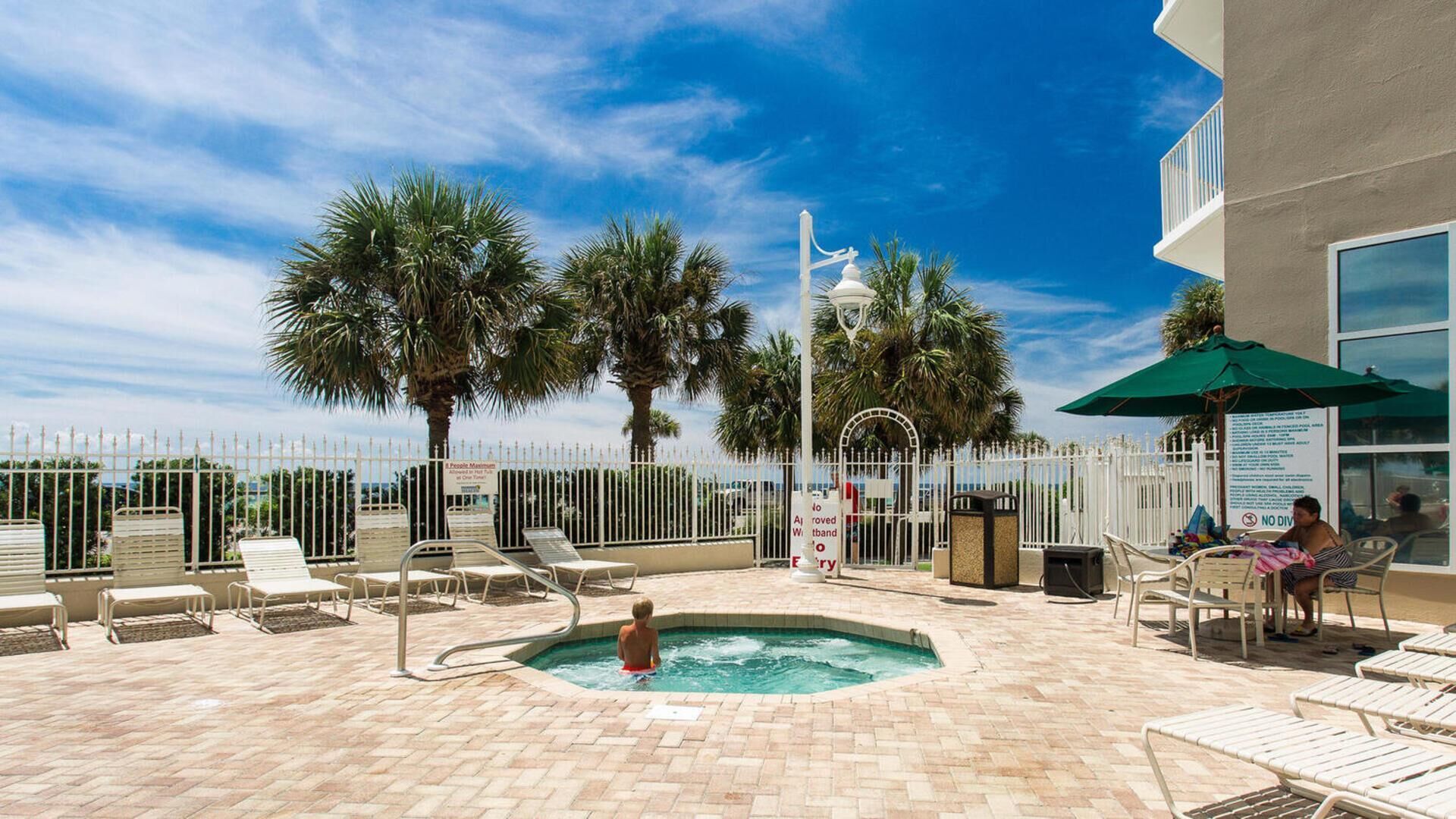 A pool area with lounge chairs, a hot tub, and palm trees.