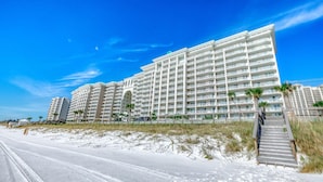 Ein mehrstöckiges Hotel mit Balkonen, nahe einem Strand mit einem sandigen Weg zum Eingang.