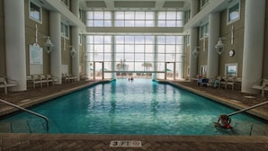 Ein überdachter Pool mit Panoramafenstern, Liegestühlen und Blick ins Freie.