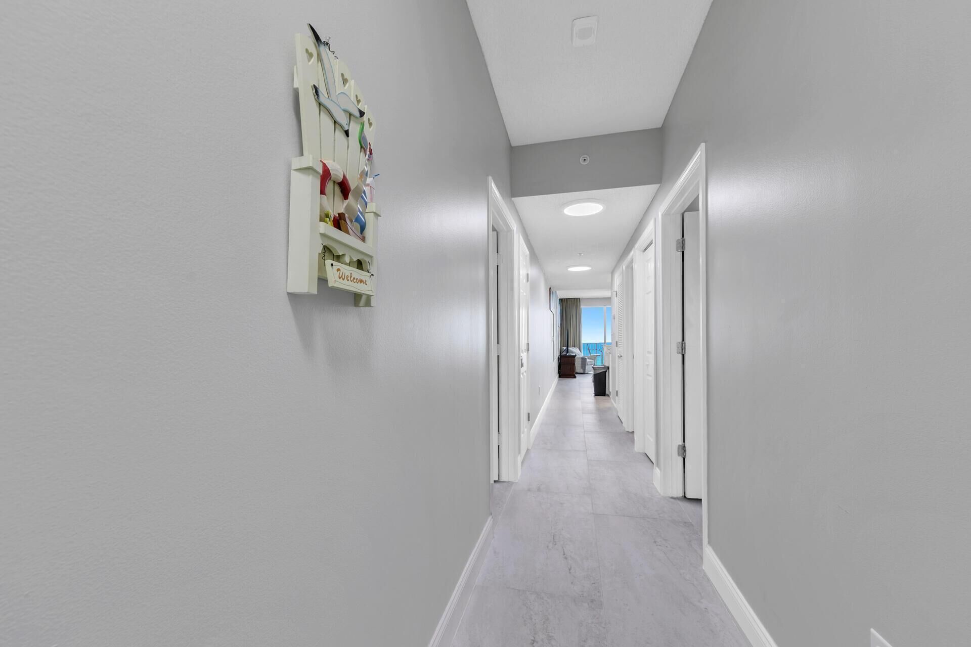 Un couloir avec une porte blanche au fond, un panneau d’accueil et un élément décoratif fixé au mur.