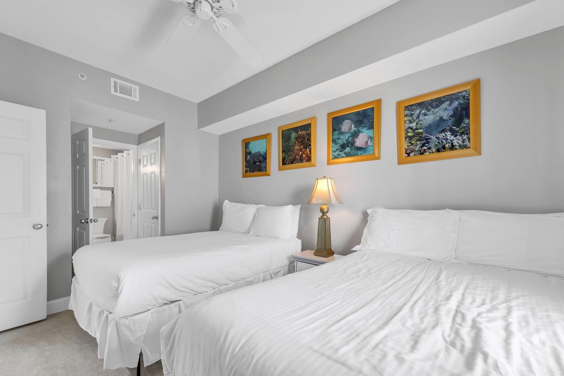 A hotel room with two beds, a ceiling fan, and four framed pictures on the wall.