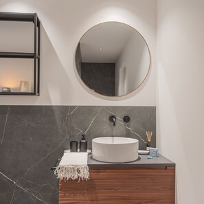 Een moderne badkamer met een ronde spiegel, een witte wastafel en een donker marmeren aanrechtblad.