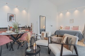 Una moderna camera d'albergo con zona pranzo, un letto con copripiumino grigio e rosa e un grande specchio.