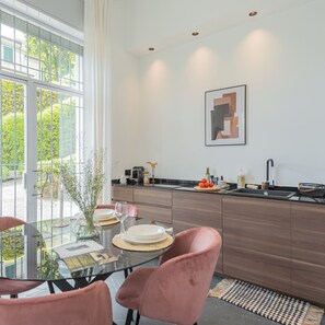 Una cucina moderna con un tavolo da pranzo in vetro, sedie rosa e vista sul verde circostante.