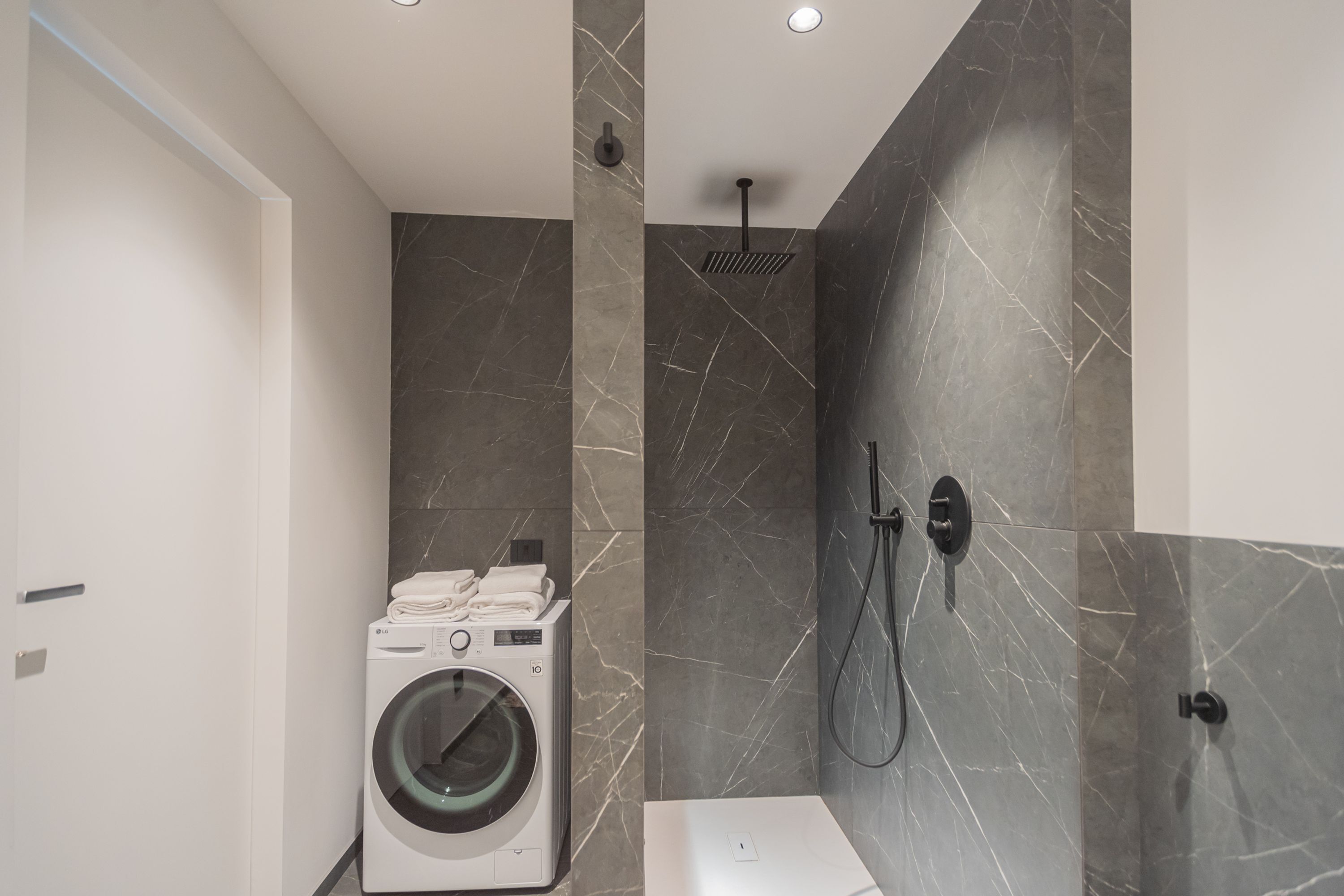 Une salle de bain moderne équipée d’un lave-linge, d’une douche et de murs en marbre.