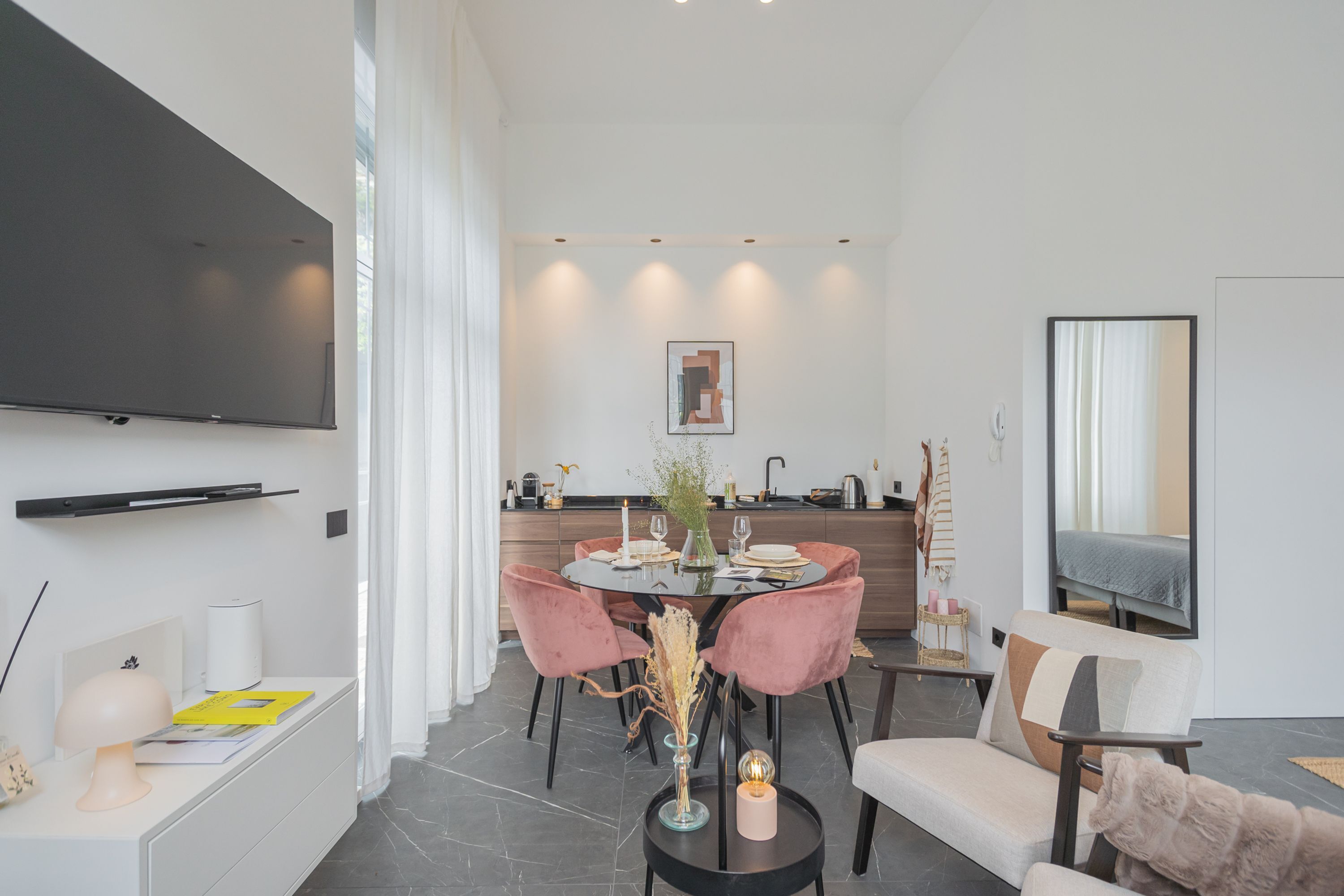 Un salon moderne avec un coin repas, un téléviseur à écran plat fixé au mur et une cuisine en arrière-plan.