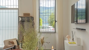 A room with a large window, a flat-screen TV, a desk with a lamp, and a chair. - Piccola Como Lotus With 1 Bathrooms (Carate Urio)