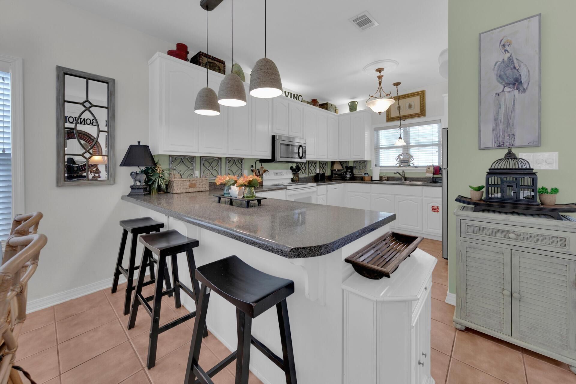 A modern kitchen with white cabinets, a large island with bar stools, pendant lighting, and a view of the living area.