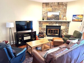 Una sala de estar con chimenea de piedra, sofás de cuero, un televisor y una mesa de centro.