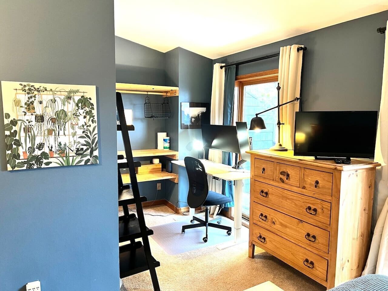A room with a desk, chair, dresser, and a television.
