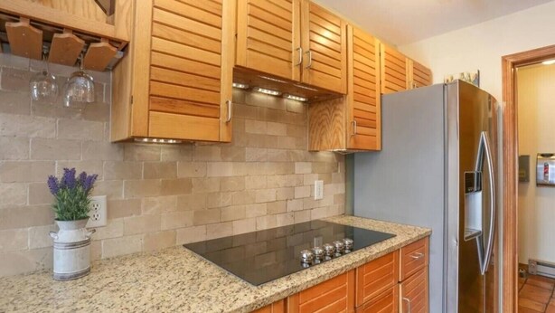 A kitchen with wooden cabinets, a granite countertop, a stainless steel refrigerator, and a built-in stove.