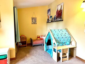 Un dormitorio infantil con una cama, un escritorio pequeño, una estantería y una tienda de juegos.