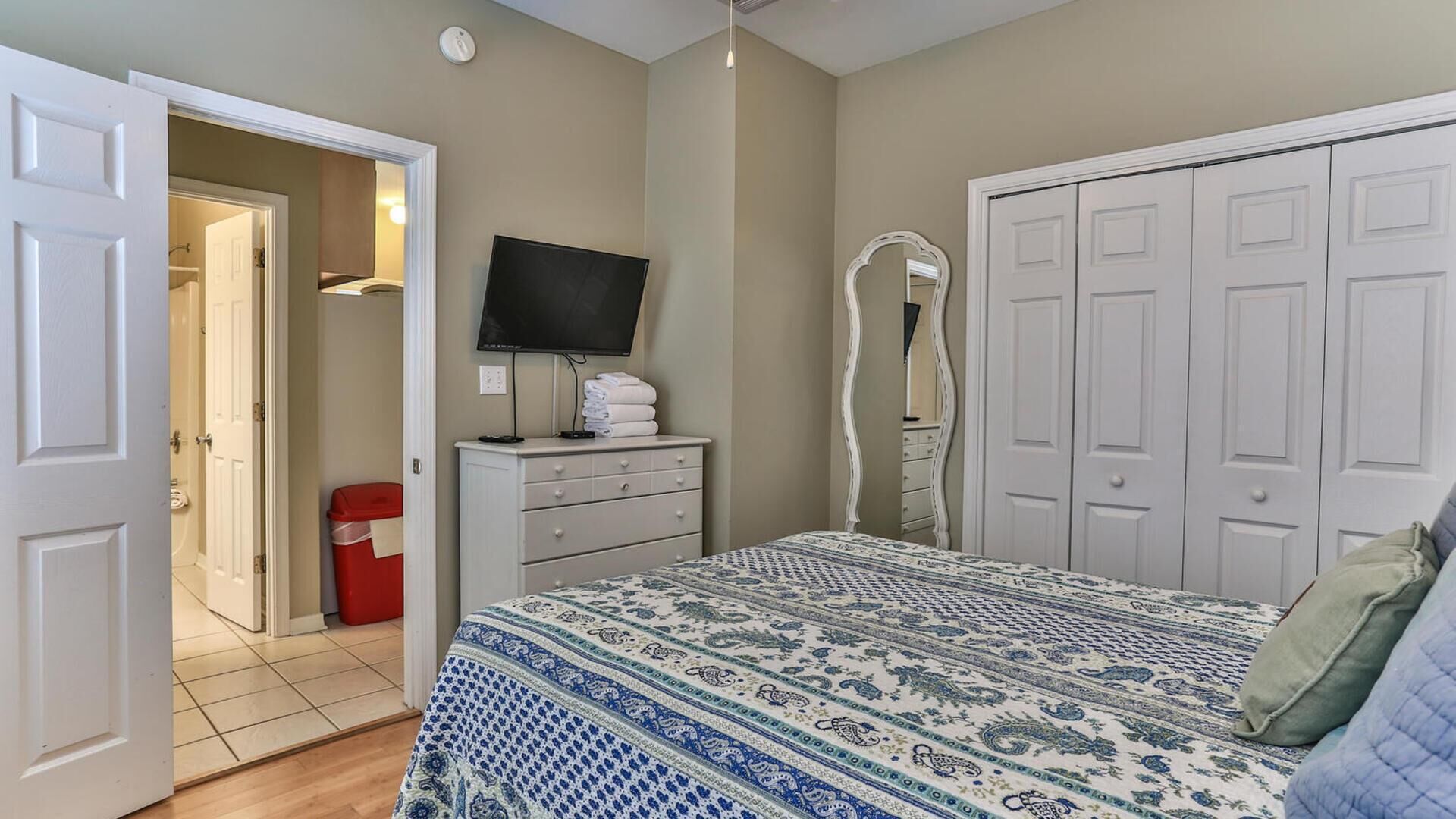 A bedroom with a bed, a TV, a dresser, a mirror, and a wardrobe.