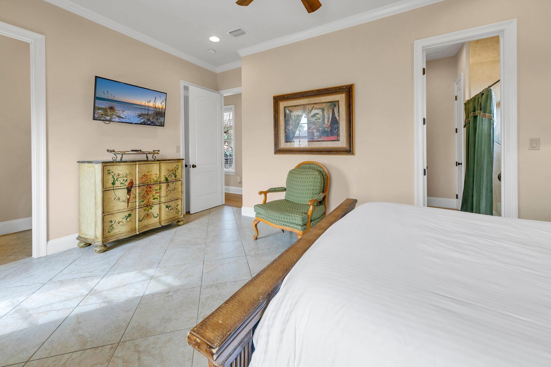 A bedroom with a large bed, a dresser, a chair, and two doors leading to other rooms.