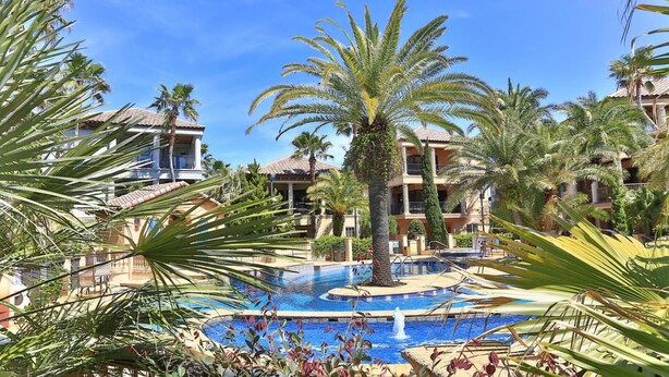 A resort with a central swimming pool, palm trees, and multi-story buildings with balconies. - Tuscany (Miramar Beach)