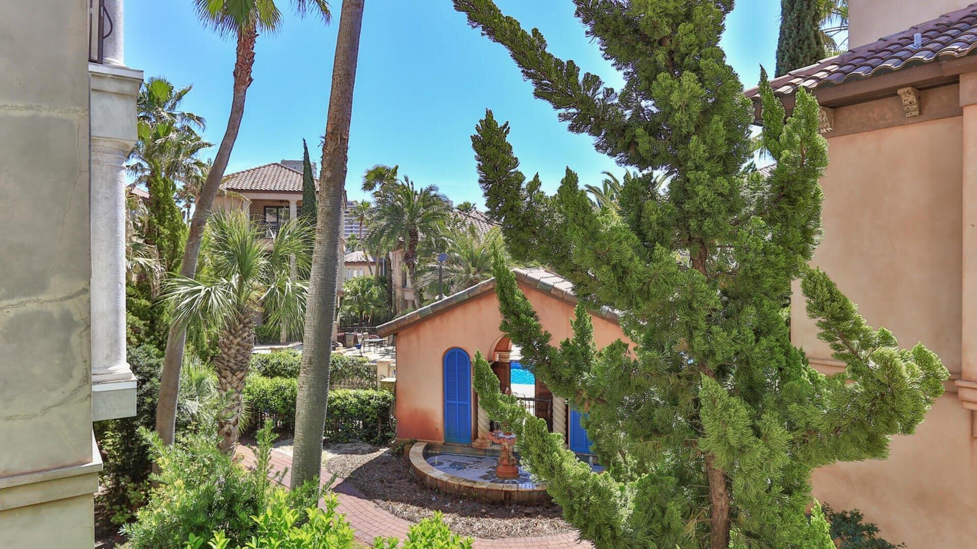 A courtyard with a fountain, palm trees, and a building with blue shutters.