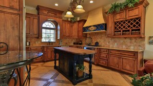 A kitchen with wooden cabinets, a central island, a window, and a wine rack. - Tuscany (Miramar Beach)