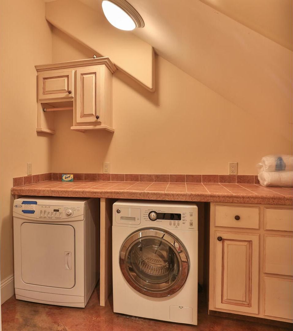 A laundry room with two washing machines, a countertop, and cabinets.