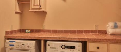 A laundry room with two washing machines, a countertop, and cabinets.