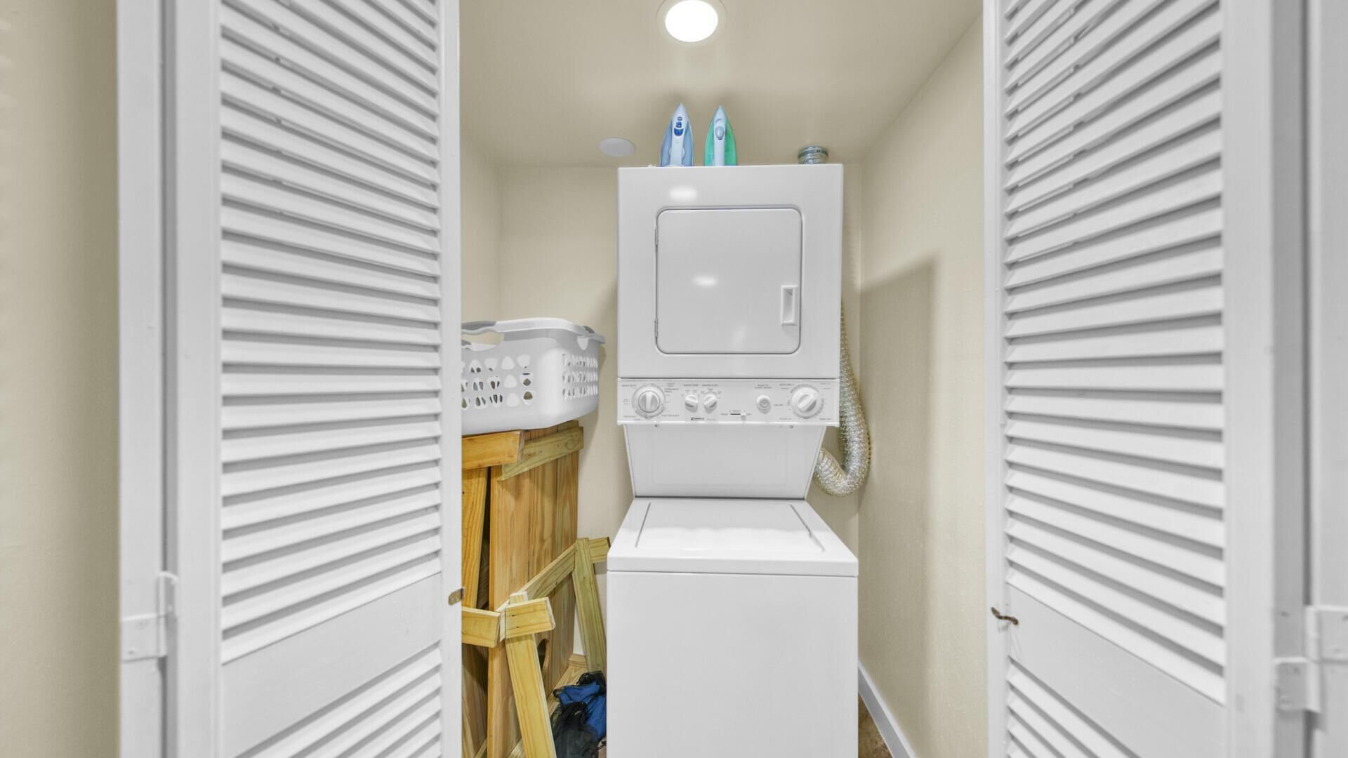 A laundry room with a stacked washer and dryer, wooden shelves, and a white laundry basket.