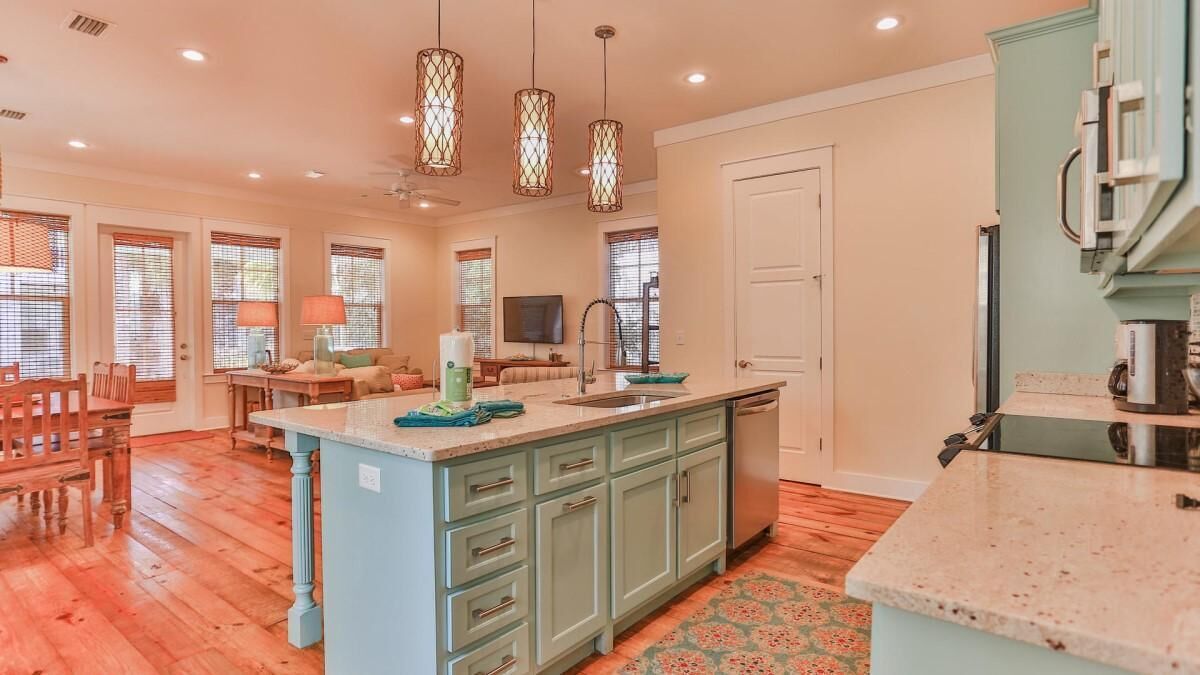 Una cocina amplia con una isla central, piso de madera e iluminación colgante.
