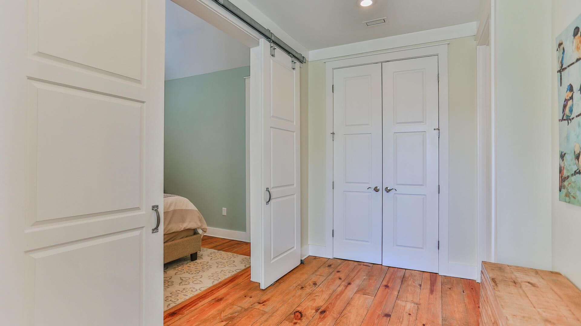 Un pasillo con suelo de madera, puertas blancas y una cama con una manta color beige.