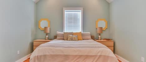 A bedroom with a sloped ceiling, a large bed with a beige bedspread, two nightstands with lamps, and a window with blinds.