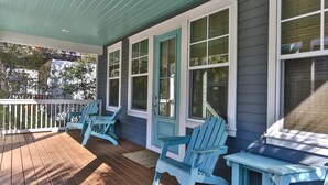 Une véranda avec un plancher en bois, une balustrade blanche et trois chaises Adirondack bleues.
