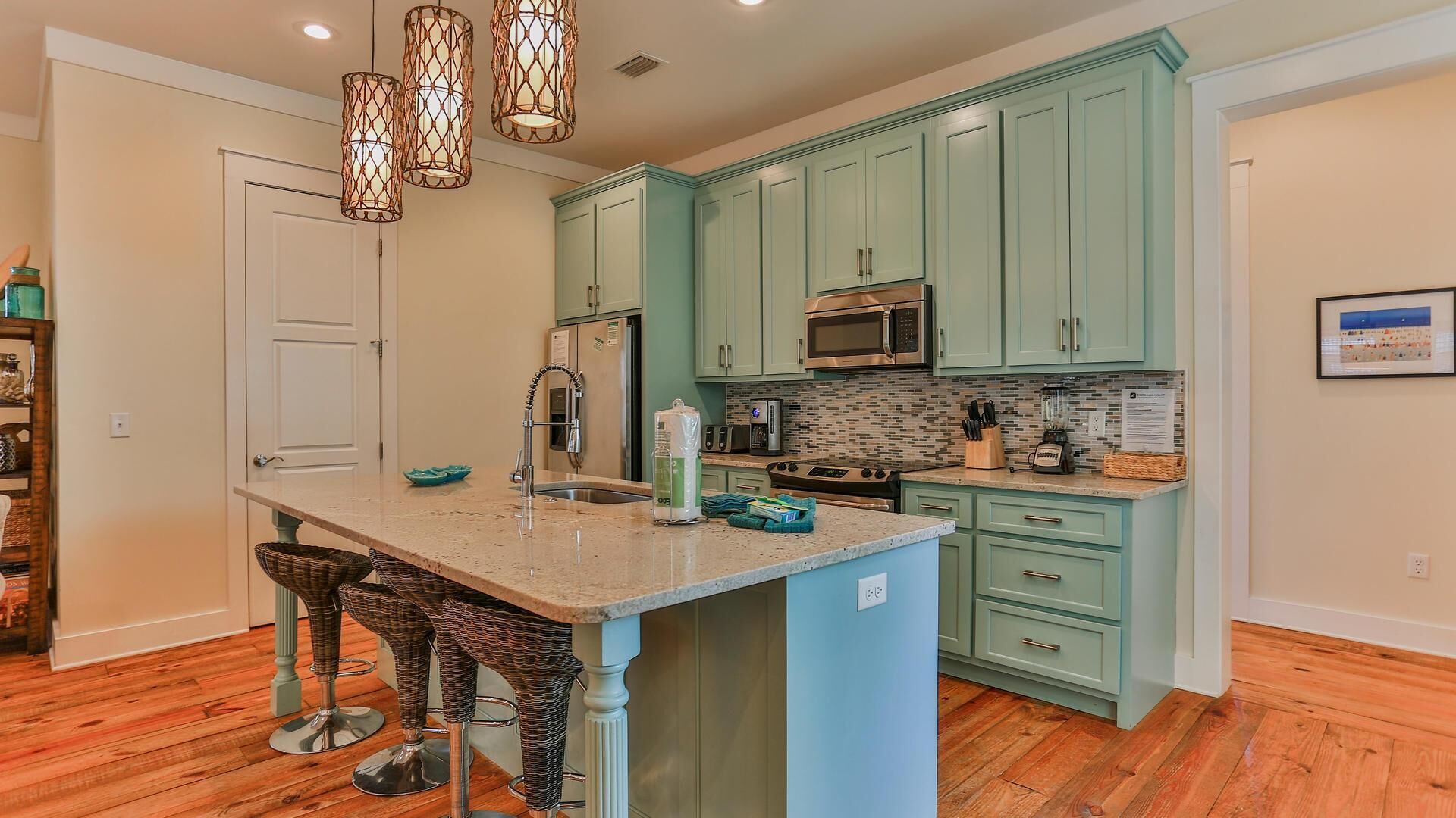 A kitchen with teal cabinets, a central island with stools, a microwave, and a sink.