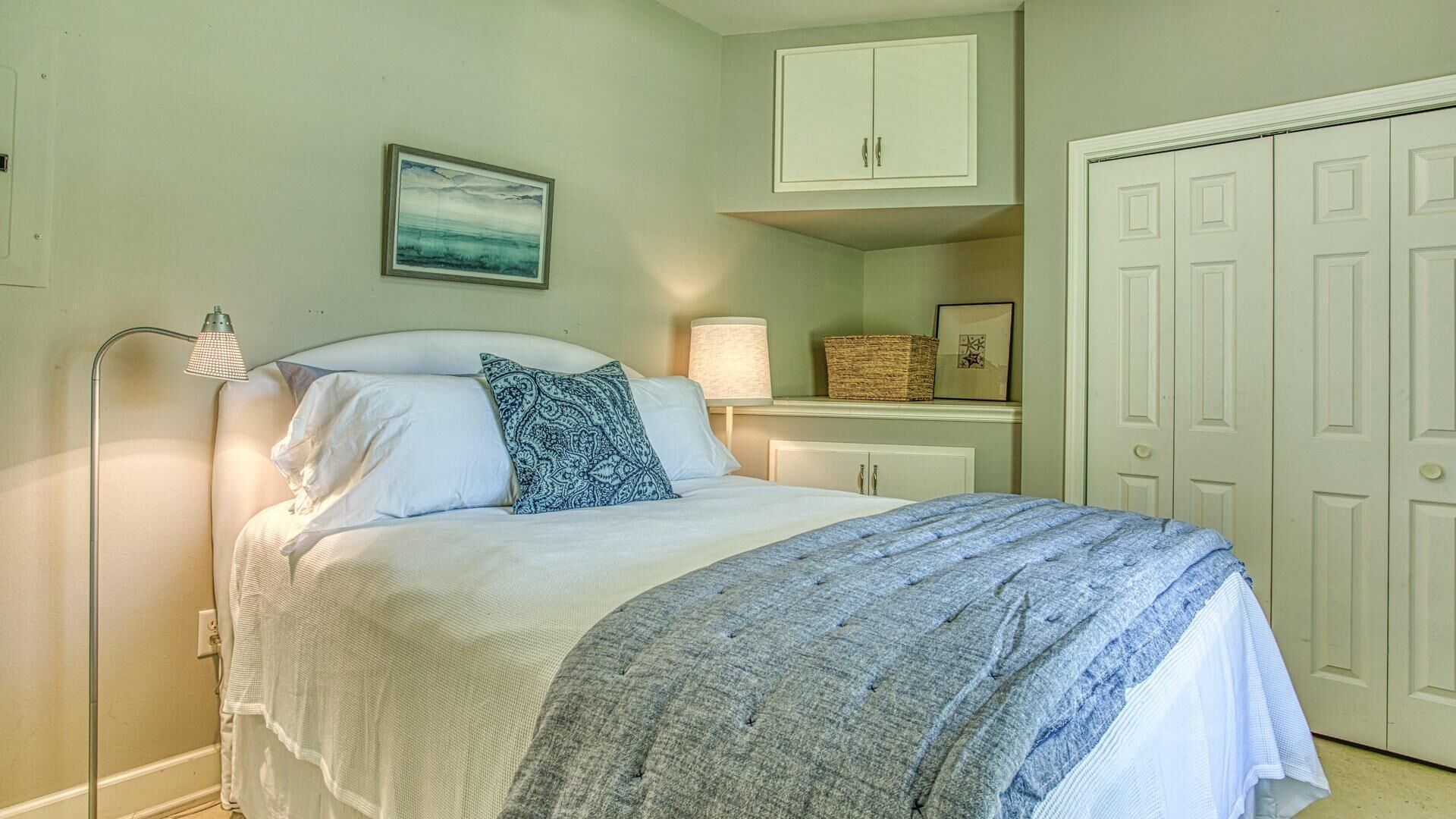 A neatly made bed with a patterned throw, a bedside lamp, and a framed picture on the wall.