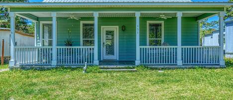 A green house with a porch, a front door, and a number '15' on the wall.