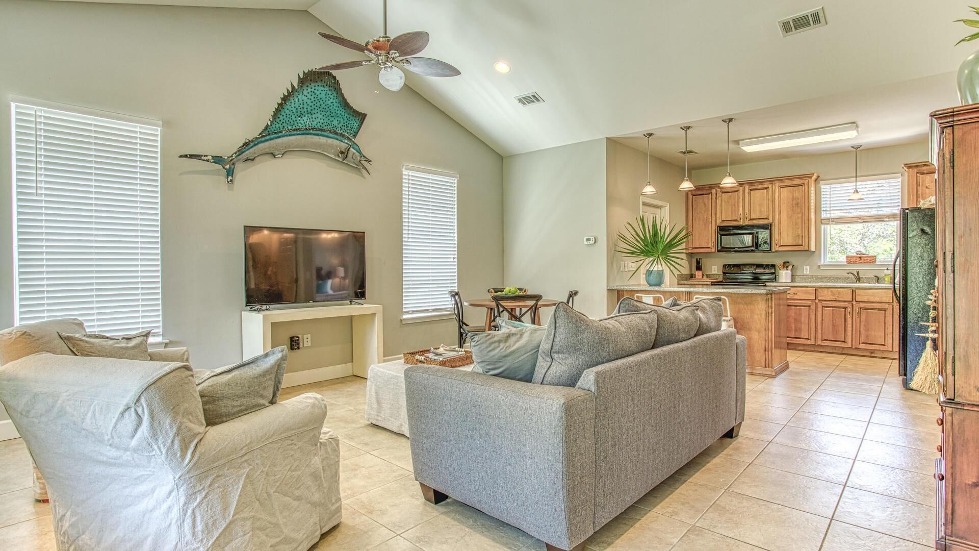 A spacious living room with a gray sofa, a television, and a ceiling fan.