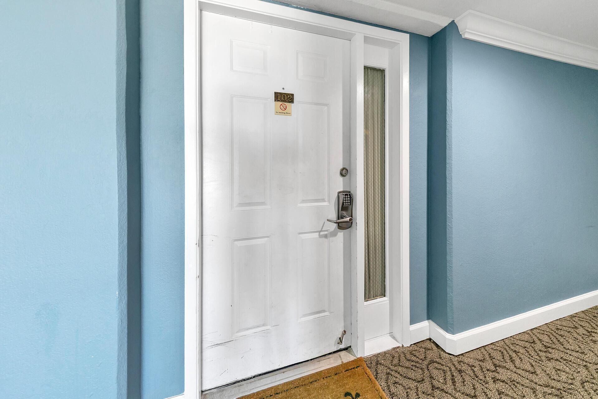 A white door with a keypad lock and a no-smoking sign, blue walls, and a textured carpet.