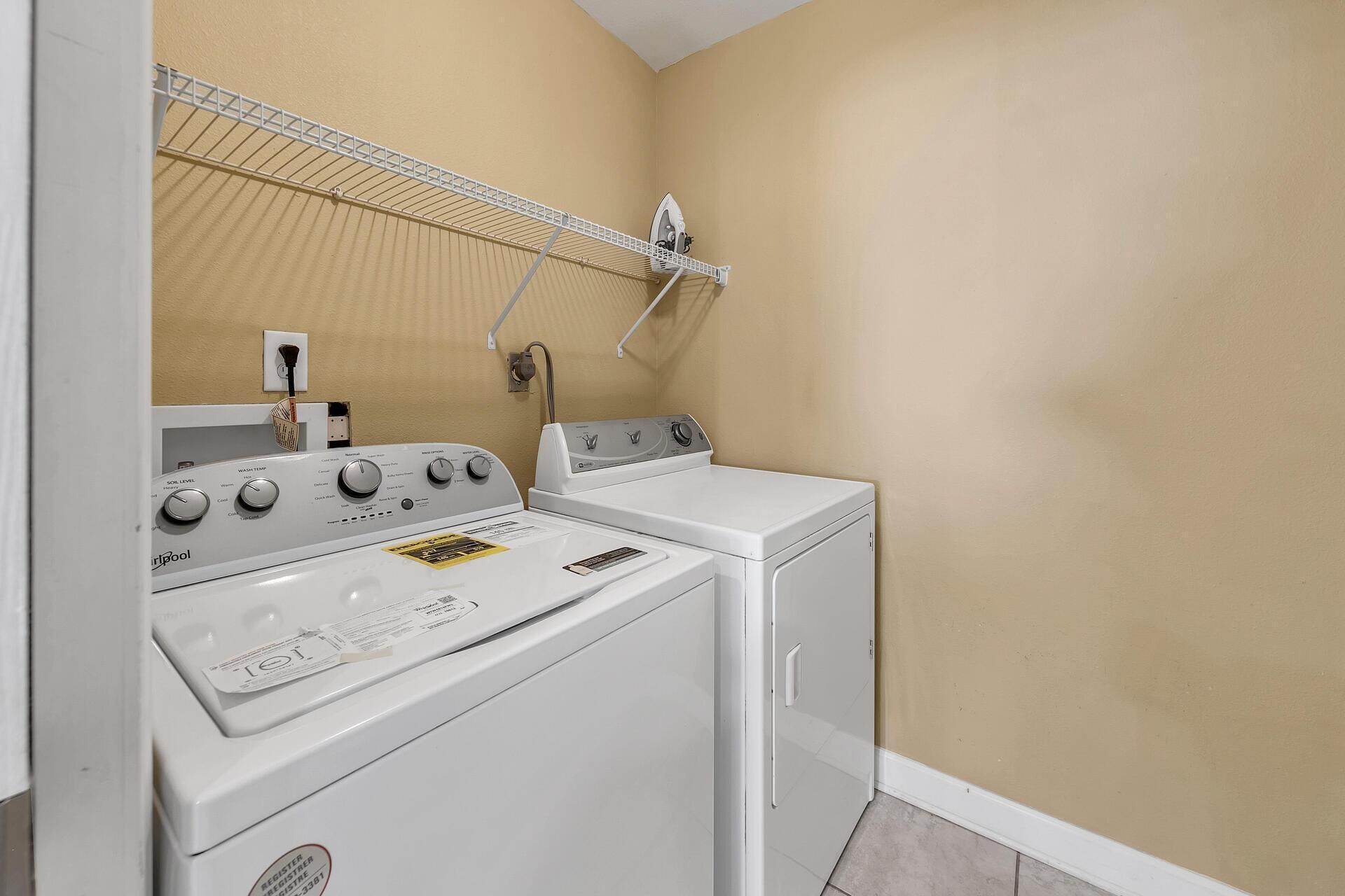A laundry room with a front-loading washer and dryer, a drying rack, and a wall-mounted ironing board.