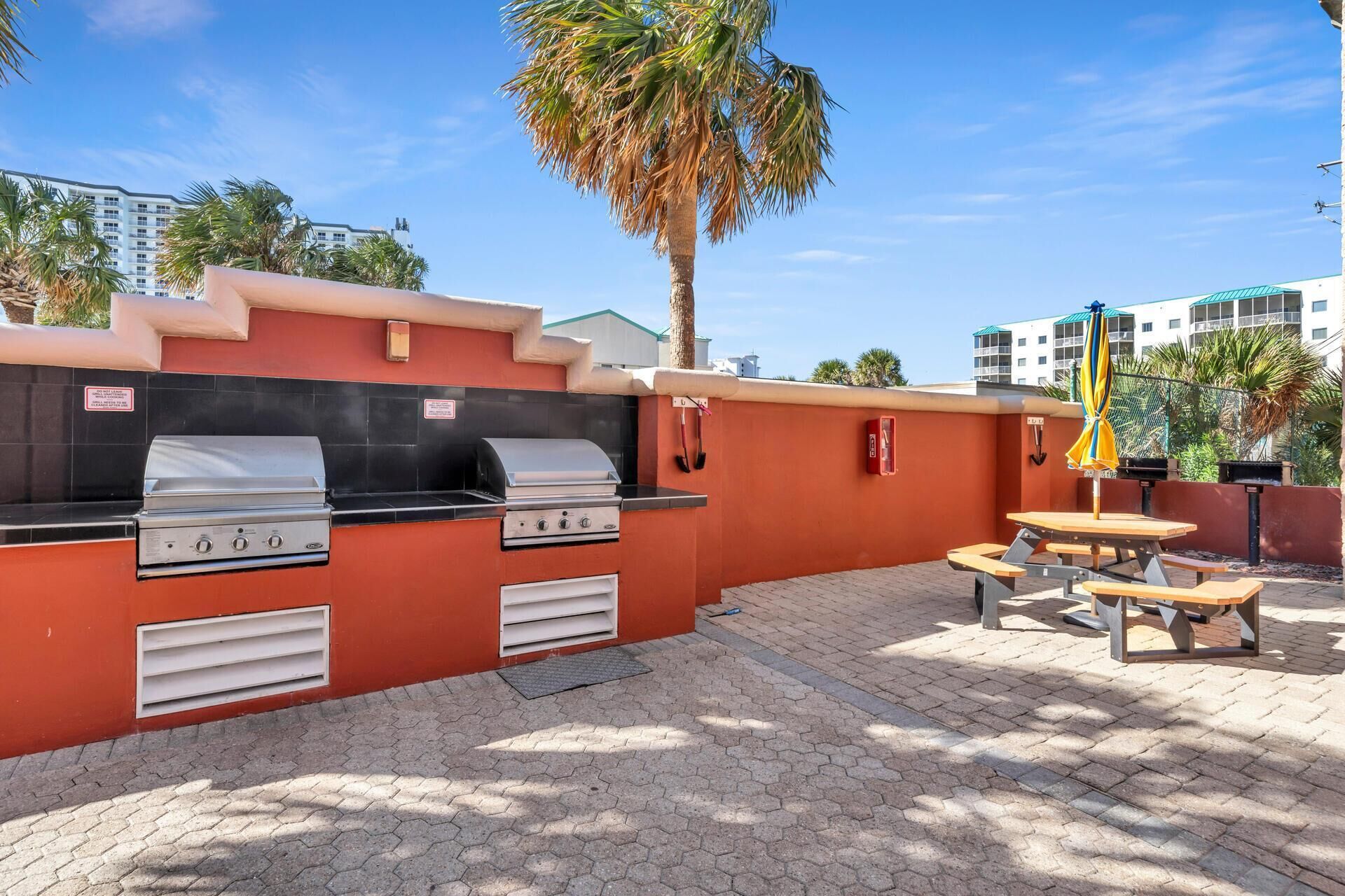 An outdoor barbecue area with two gas grills, a picnic table, and a fire extinguisher.
