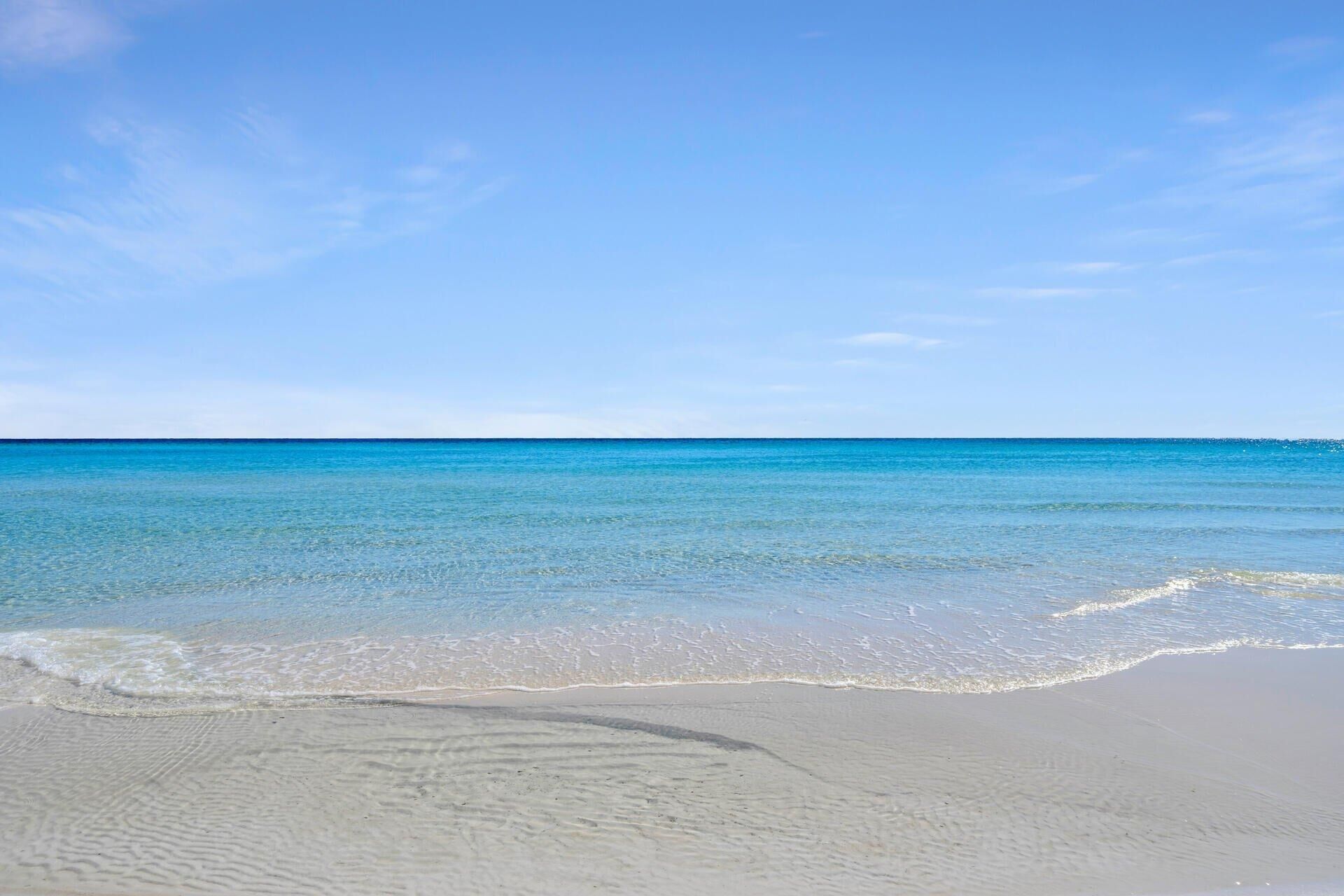 A beach with clear blue water and a sandy shore.