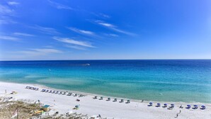 A beach with clear blue water, a boat in the distance, and rows of umbrellas along the shore. - Destin Towers 111 (Destin)