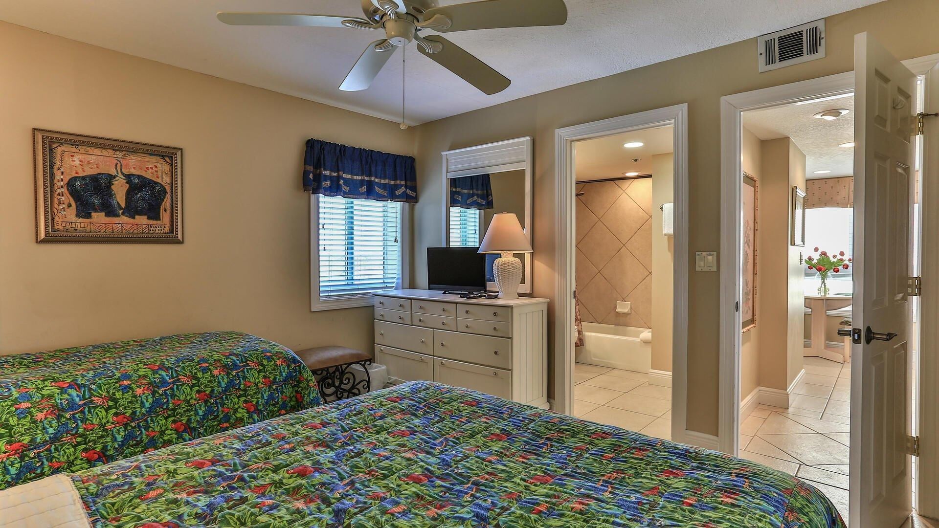 Une chambre avec deux lits, une commode, un téléviseur et un ventilateur de plafond.