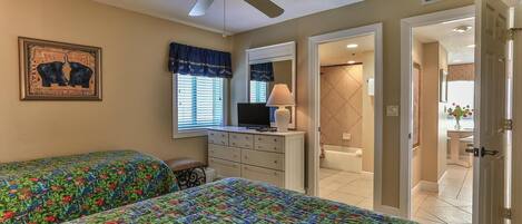 Une chambre avec deux lits, une commode, un téléviseur et un ventilateur de plafond.
