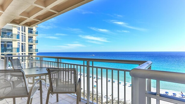 A balcony with a view of the ocean and beach, featuring a table and chairs. - Destin Towers 111 (Destin)