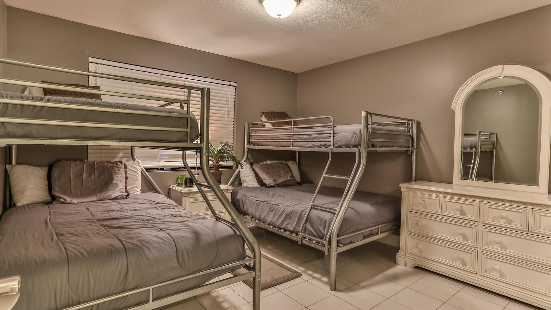 Une chambre de dortoir avec des lits superposés, une commode, un miroir et une petite plante.