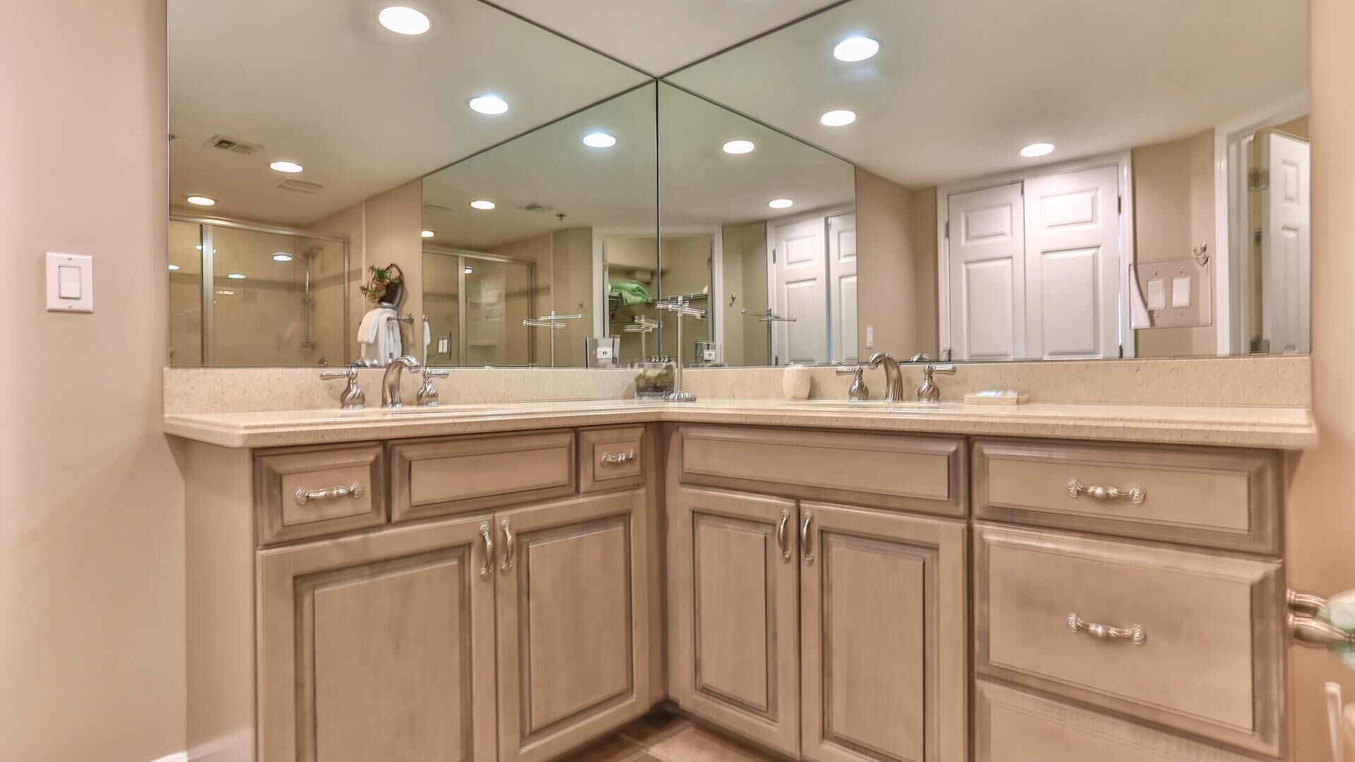 Une salle de bain dotée d’un grand miroir, de deux lavabos et de meubles de rangement de couleur beige.
