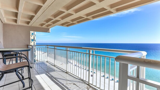 A balcony with a view of the ocean, a table, and chairs. - Destin Towers 142 (Destin)