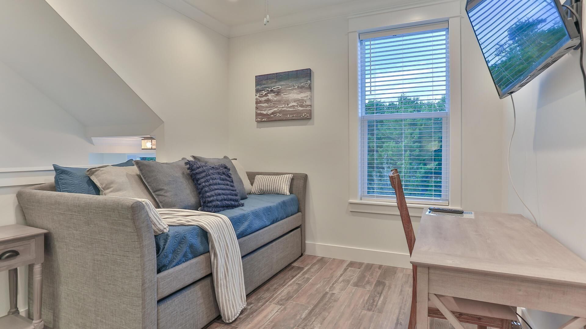 A modern living room with a grey sofa, a wooden coffee table, and a large window with blinds.