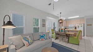 A modern living room with a sofa, a round coffee table, and a dining area with a wooden table and chairs. - Pops Place (Santa Rosa Beach)