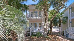A two-story building with a porch, surrounded by palm trees and a pathway. - Pops Place (Santa Rosa Beach)