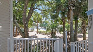 A porch with white railings overlooking a landscaped area with trees and a pathway. - Pops Place (Santa Rosa Beach)