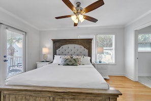 A bedroom with a large bed, wooden headboard, two bedside tables with lamps, a ceiling fan, and large windows with blinds. - La Bella Vita (Santa Rosa Beach)