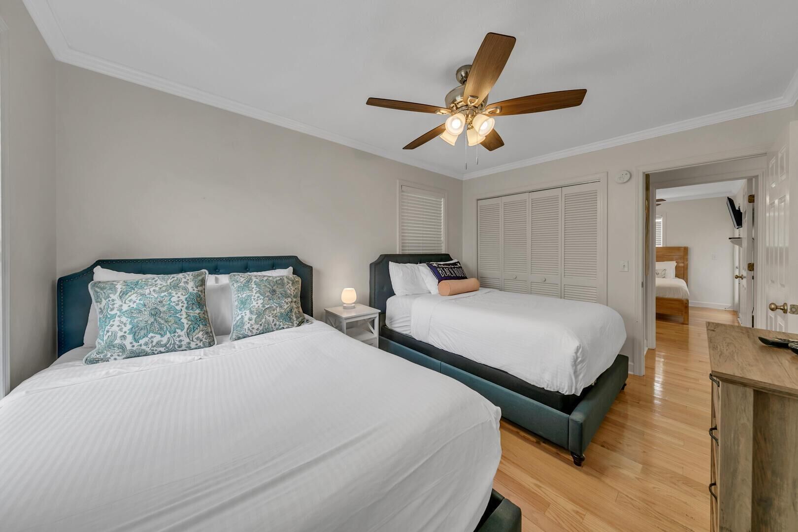 A bedroom with two beds, a ceiling fan, a nightstand with a lamp, and a wooden dresser.