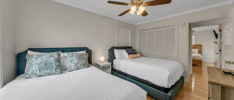 A bedroom with two beds, a ceiling fan, a nightstand with a lamp, and a wooden dresser.